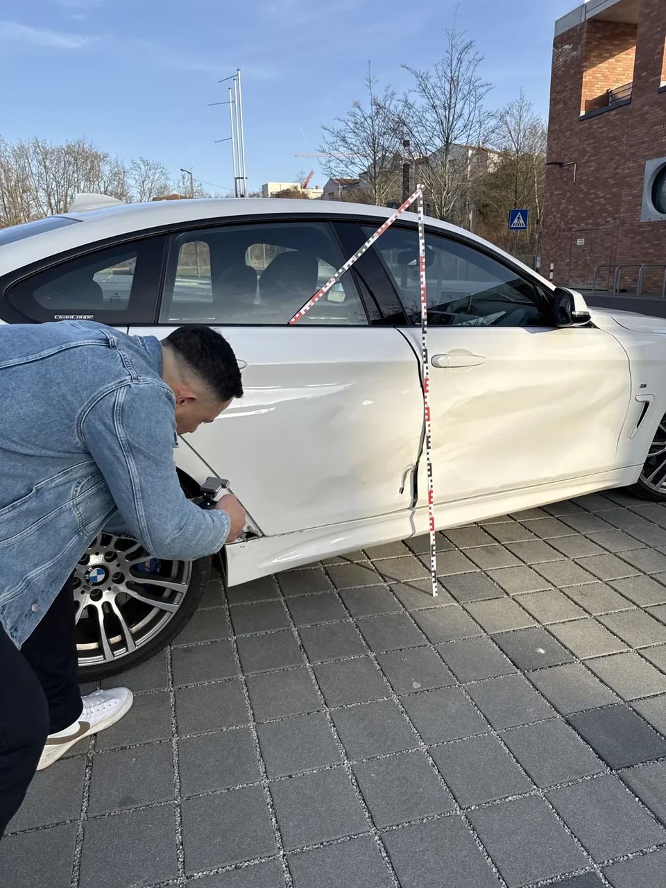 Oleg Tashin bei der Untersuchung der Fahrzeugseite eines weißen BMW